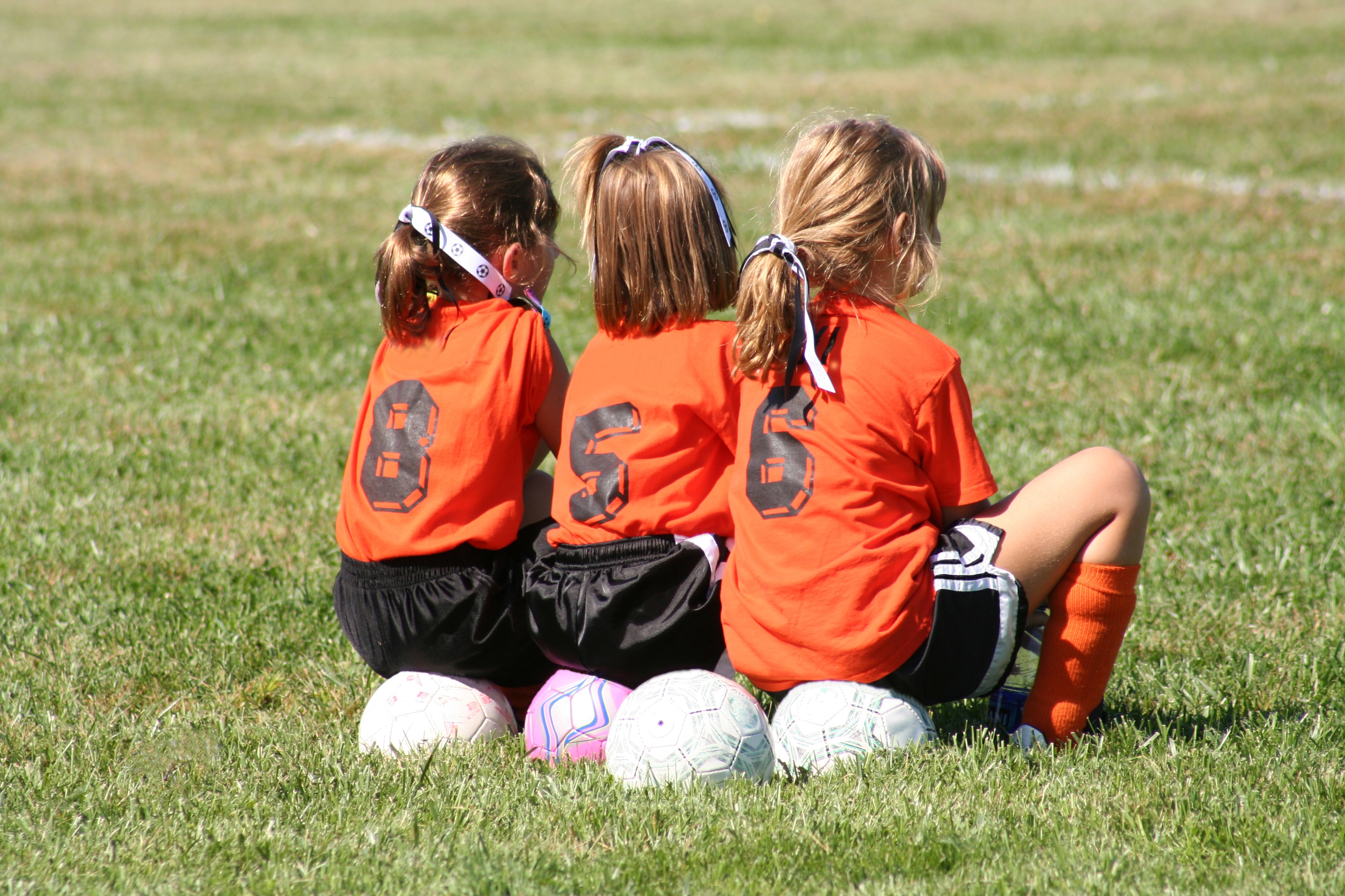Three young girls sitting on soccer balls on the field